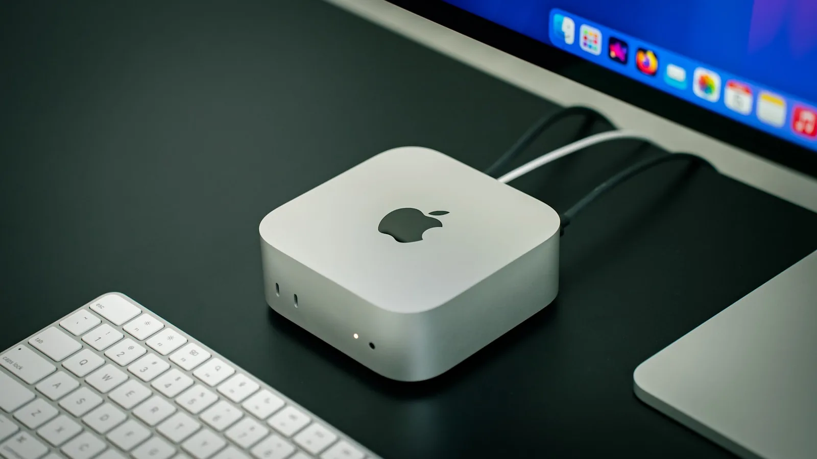 A Mac Mini on a desk beside an Apple keyboard and display — the kind of machine a Stack AI OS ships on
